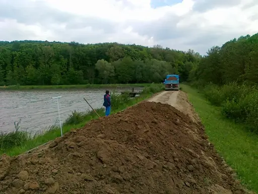 Gátépítés és partfal megerősítése víztározó mellett: teherautós földszállítás és gépi tereprendezés az Ujj Trans Kft. szakembereivel